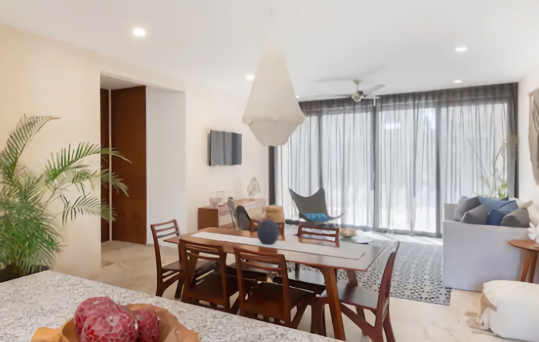 Un salon moderne avec un coin repas, de grandes fenêtres avec des rideaux, un ventilateur de plafond et une plante.