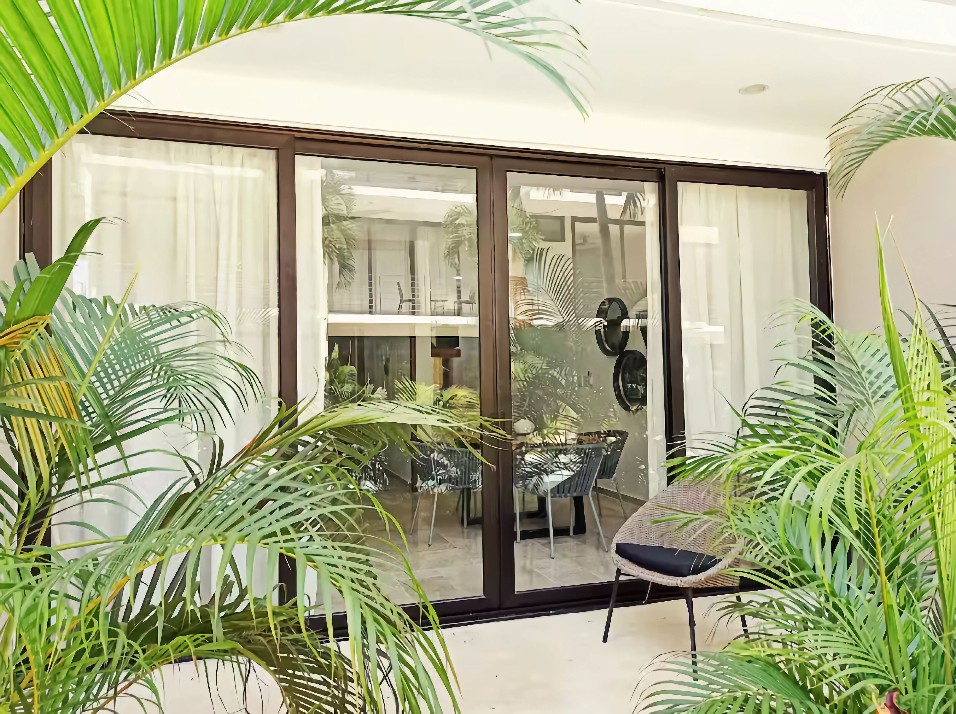 Un interior moderno con una puerta de vidrio que da a un espacio exterior, rodeado de exuberantes plantas verdes.