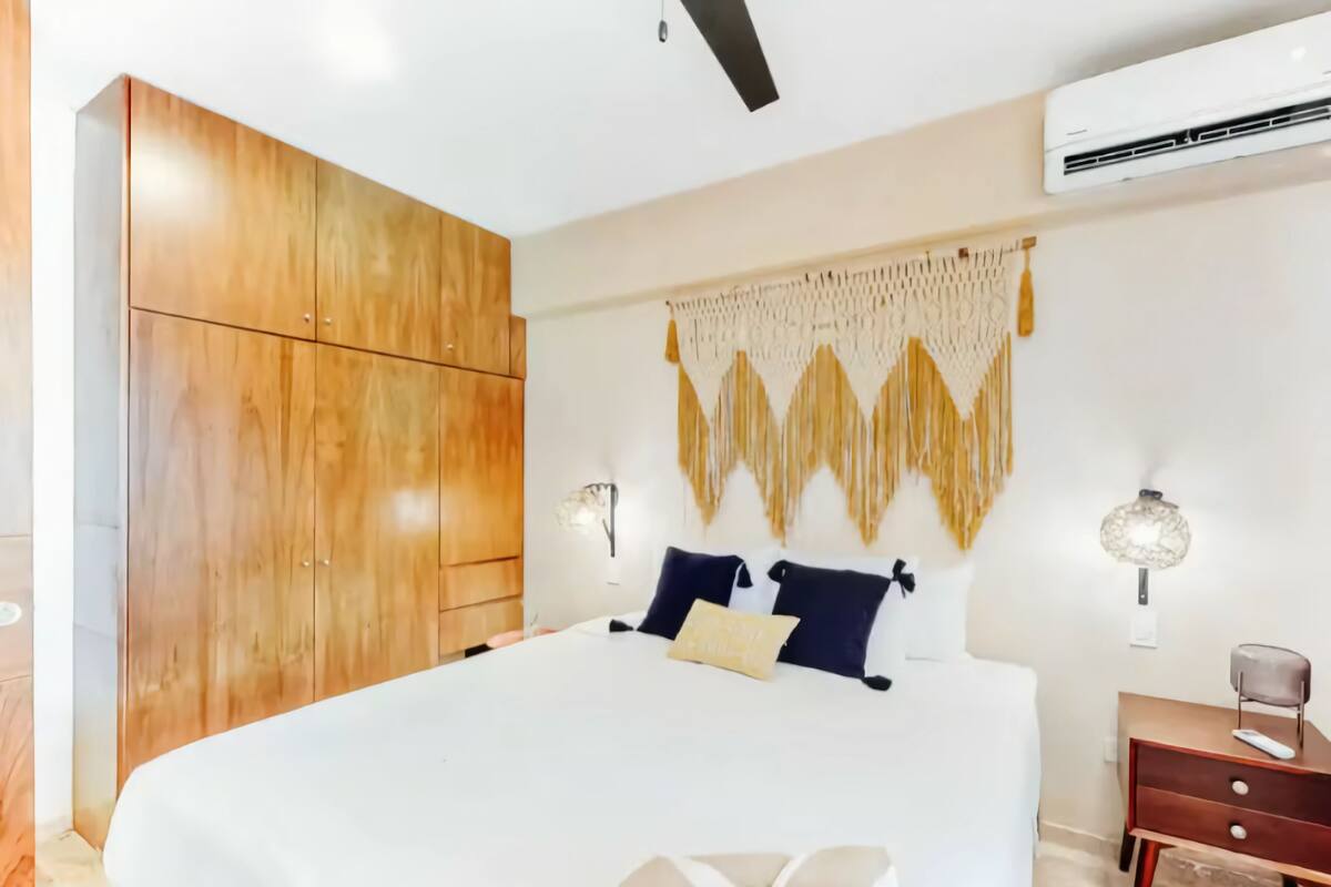 A bedroom with a large bed, wooden wardrobe, wall-mounted air conditioning, and decorative wall hanging.