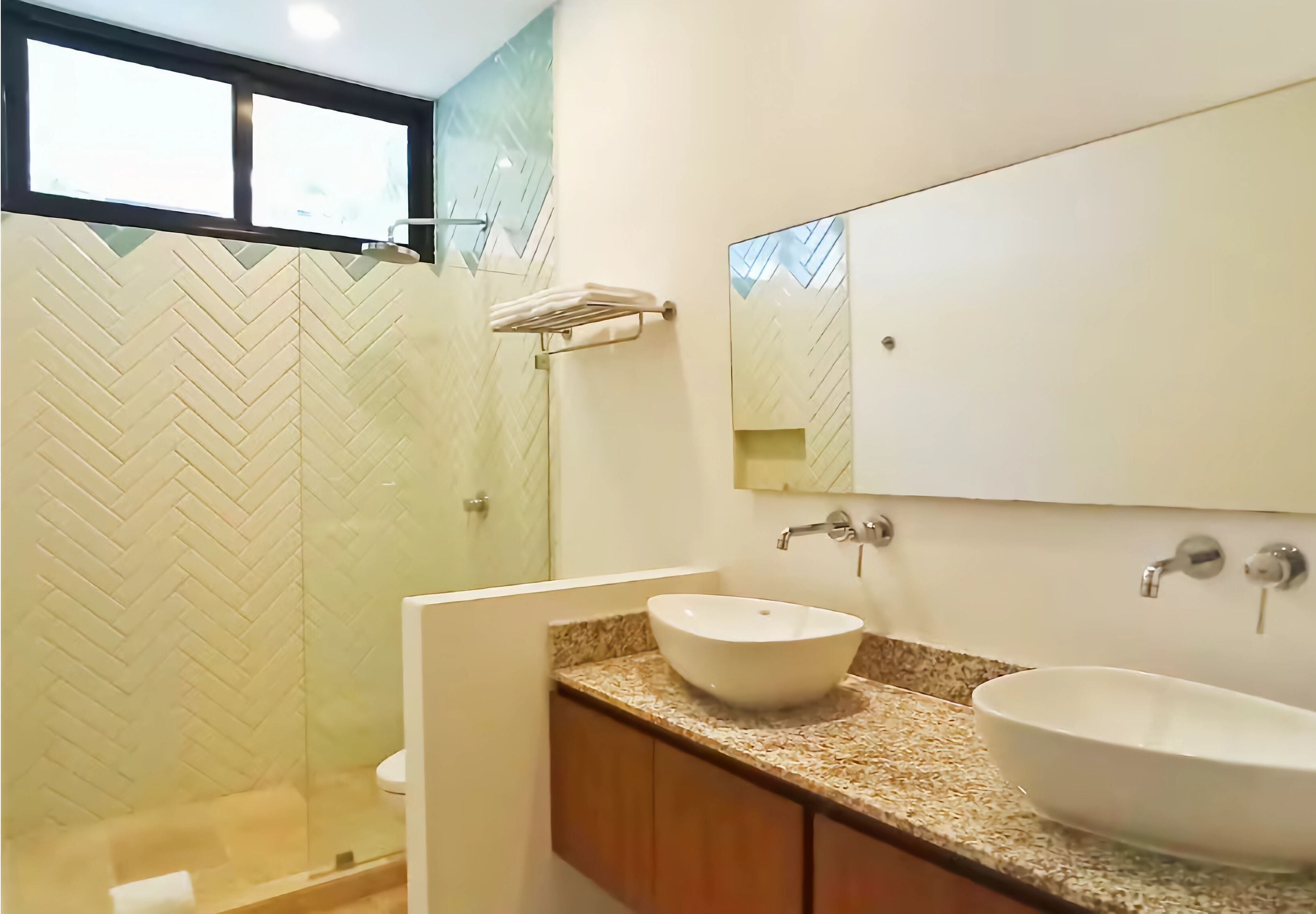 A bathroom with a herringbone-patterned wall, a large mirror, two sinks, and a towel rack.