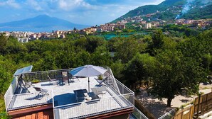 A rooftop terrace with solar panels, outdoor furniture, and a view of a coastal town. - YourHome - Relais Sant'Anna (Vico Equense)