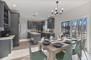 A modern kitchen with grey cabinets, a central island, and a dining area set for six. - Spacious Retreat w/ Pool, Hot Tub & Game Room (Stony Point)
