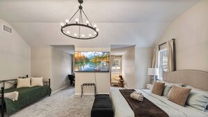 Un dormitorio con cama, un banco, un televisor y un cuadro de un lago.