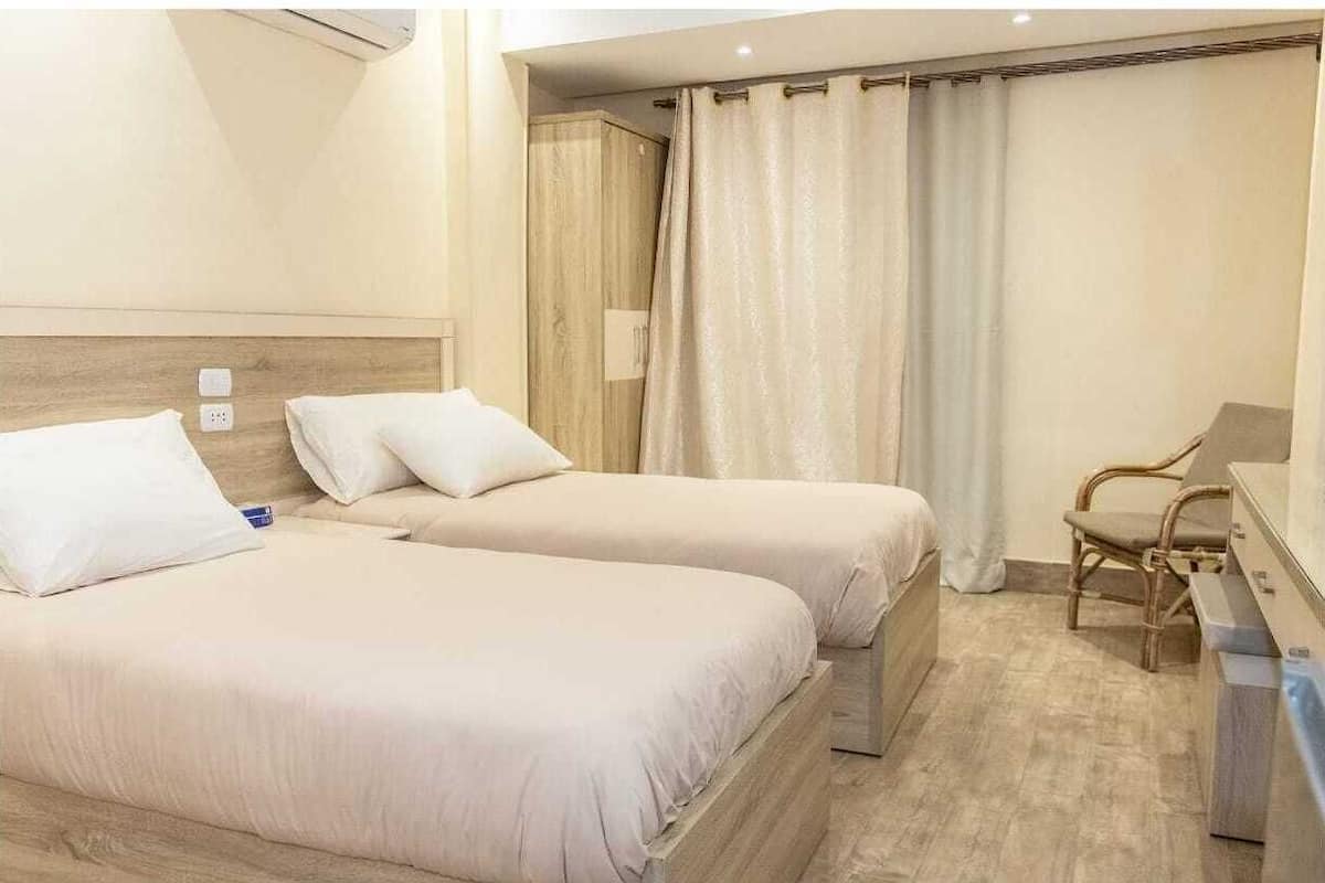 Habitación de hotel con dos camas, cabecera de madera, escritorio con silla y zona de ducha.
