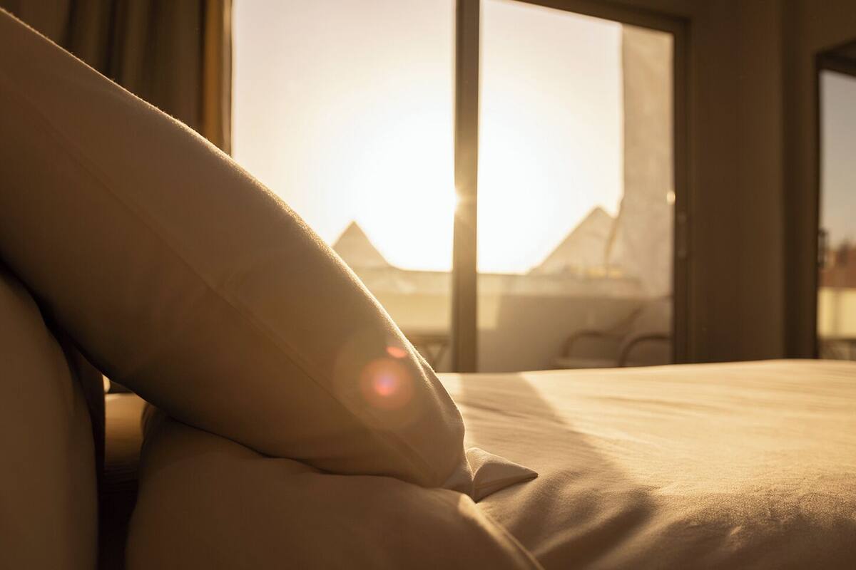 Una cama con almohada y vista a un paisaje montañoso a través de una ventana.