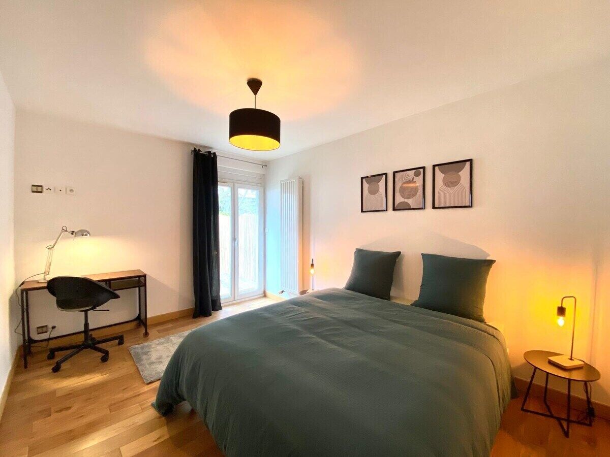 Une chambre à coucher avec un lit, un bureau, une chaise et une fenêtre avec des rideaux.
