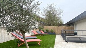 A backyard with a well-maintained lawn, a tree, and three red lounge chairs. - The Impressionist Villa (Vernon)