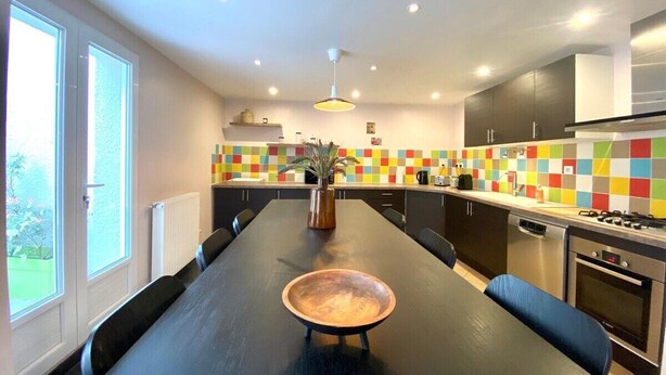 A modern kitchen with a long dining table, black cabinets, and colorful backsplash tiles. - The Impressionist Villa (Vernon)