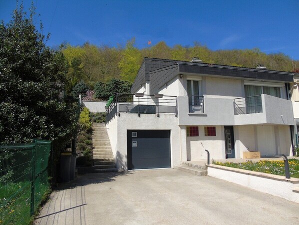 Un bâtiment moderne à deux étages, doté d’un garage, d’un escalier et d’un petit jardin agrémenté de fleurs.