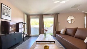 A modern living room with a sofa, a coffee table with a decorative bowl, a television, and a cabinet. - The Impressionist Villa (Vernon)