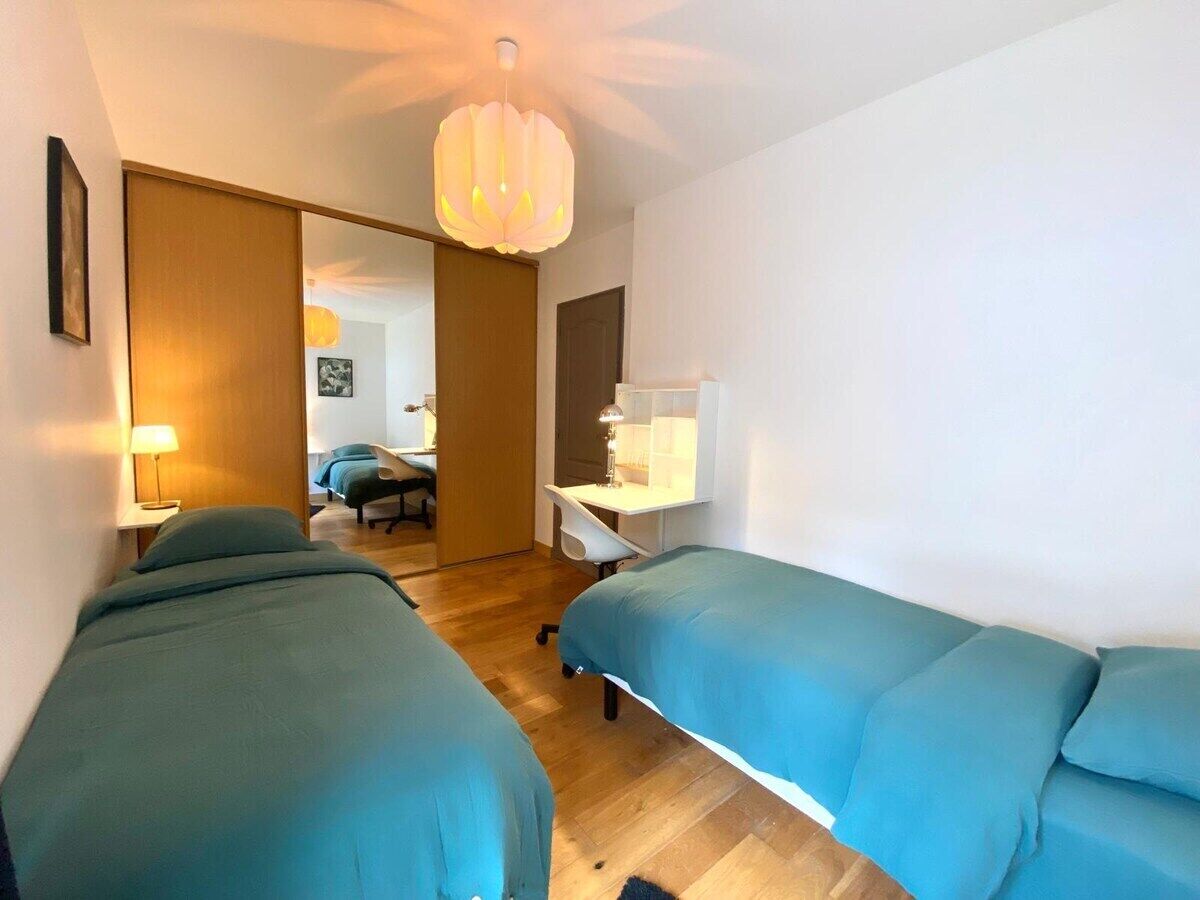 Une chambre d’hôtel avec deux lits simples, un bureau, une chaise et une grande fenêtre.
