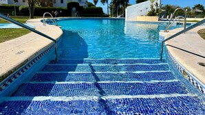 A swimming pool with blue mosaic tiles, clear water, and metal handrails.