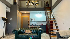 A modern living room with a green leather sofa, a coffee table, and a staircase leading to an upper level.