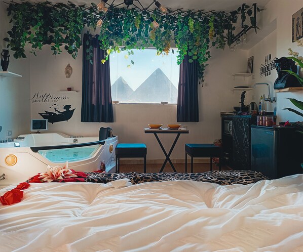 A bedroom with a bed, a small table, a bathtub, and a window with curtains.