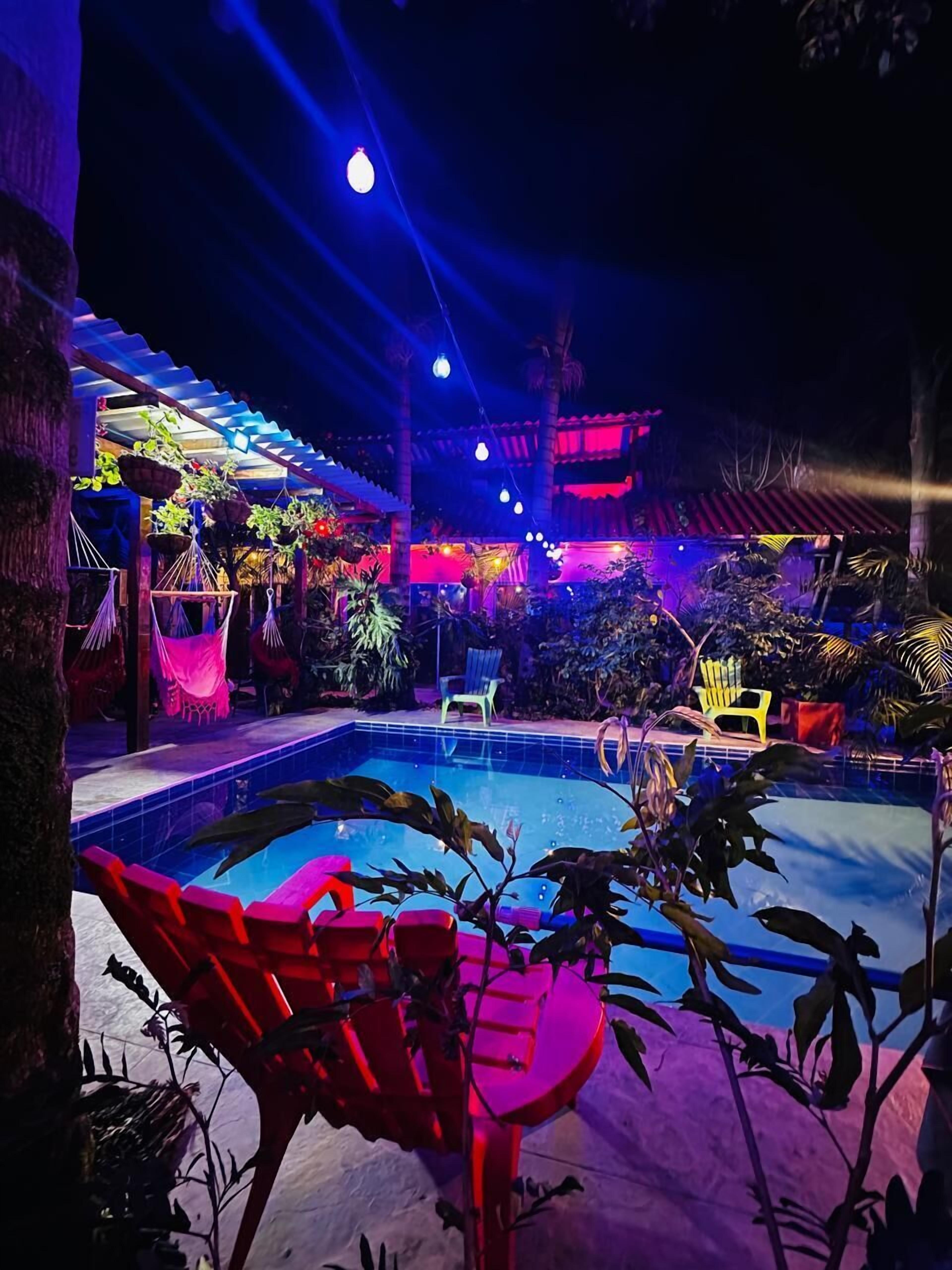A pool area with red lounge chairs, hanging plants, and a covered seating area with a red roof.