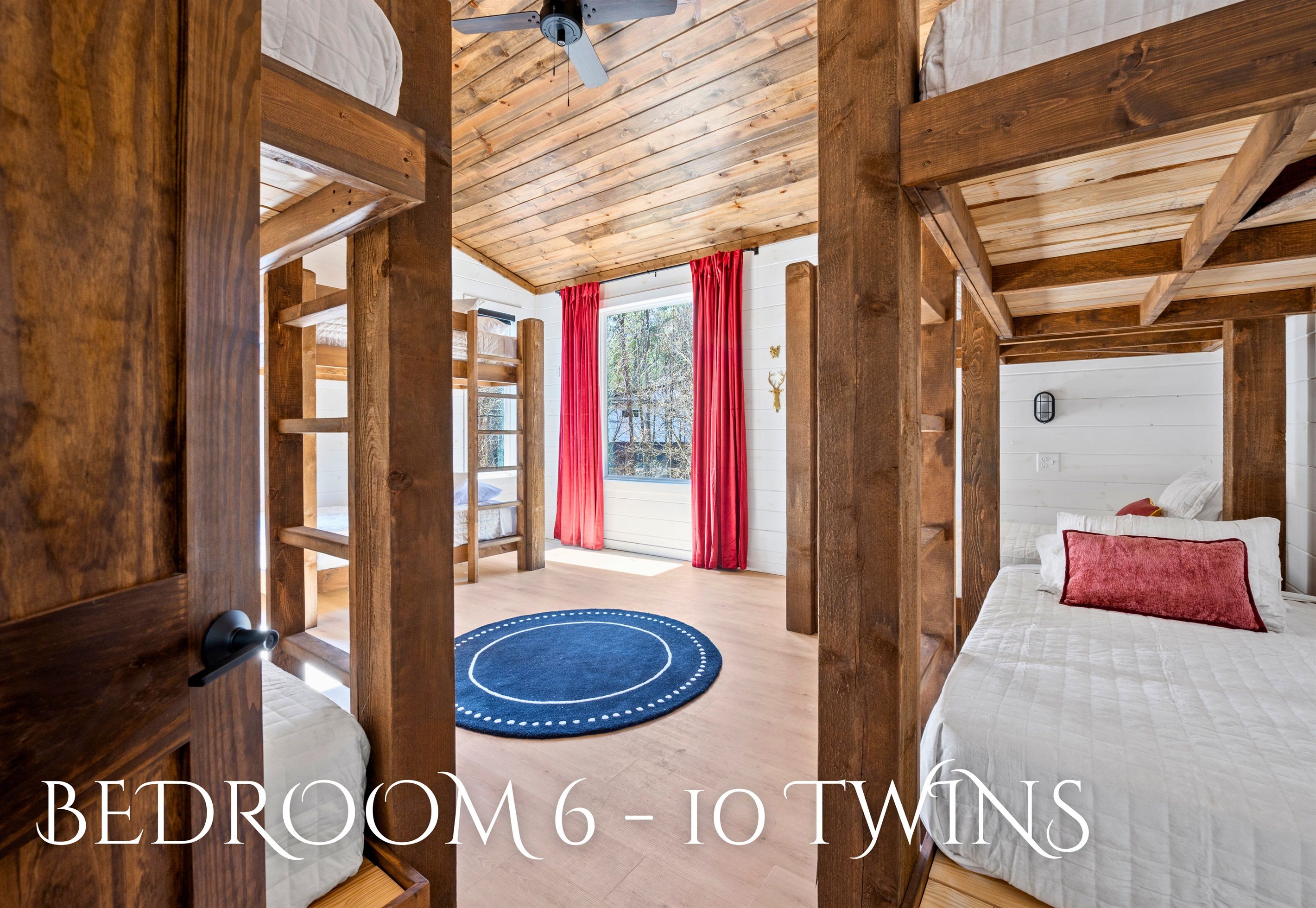 A wooden cabin bedroom with two beds, a ceiling fan, and a view of the outdoors.