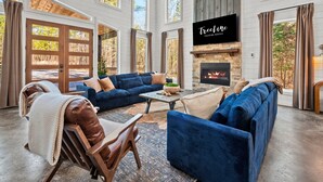 A spacious living room with a fireplace, large windows, and a television. - Kid's Play Room | Game Room | Hot Tub | Sleeps 22 (Broken Bow)
