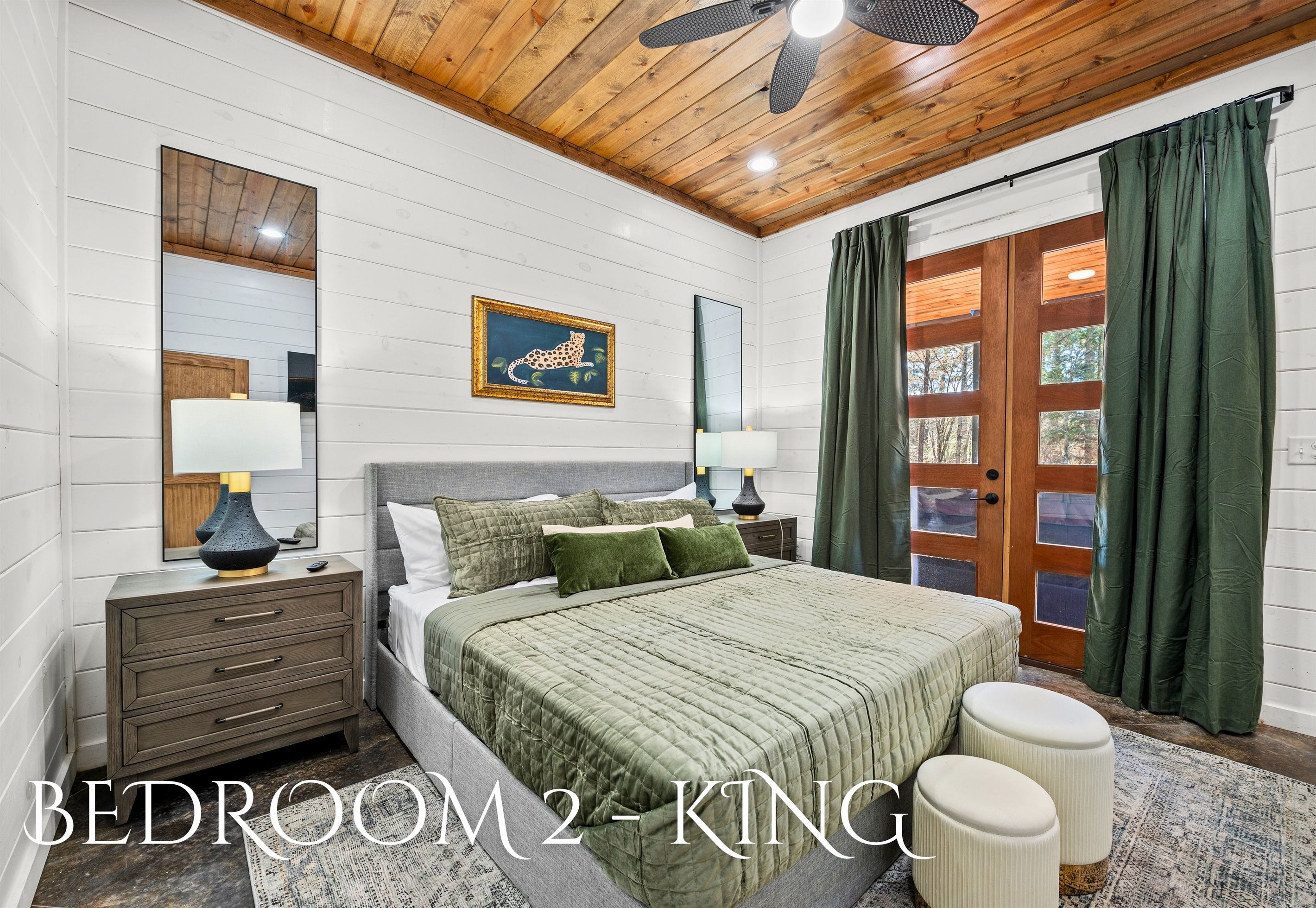 A bedroom with a bed, nightstands, a mirror, a painting, and a view of the outdoors.