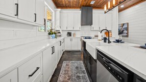 A modern kitchen with white cabinets, a wooden ceiling, and a central island with a dishwasher. - Kid's Play Room | Game Room | Hot Tub | Sleeps 22 (Broken Bow)