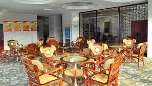 Eine Hotelhalle mit runden Tischen und Holzstühlen, einem gemusterten Boden und dekorativen Deckenleuchten.