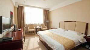Ein Hotelzimmer mit einem Bett, einem Schreibtisch mit Fernseher, zwei Sesseln, einem kleinen Tisch und einem Fenster mit Vorhängen.