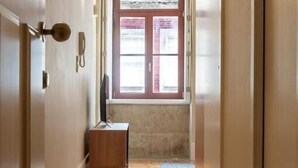 Ein Flur mit Holzboden, einer kleinen Holzbank und einem Fenster mit roten Rollläden.