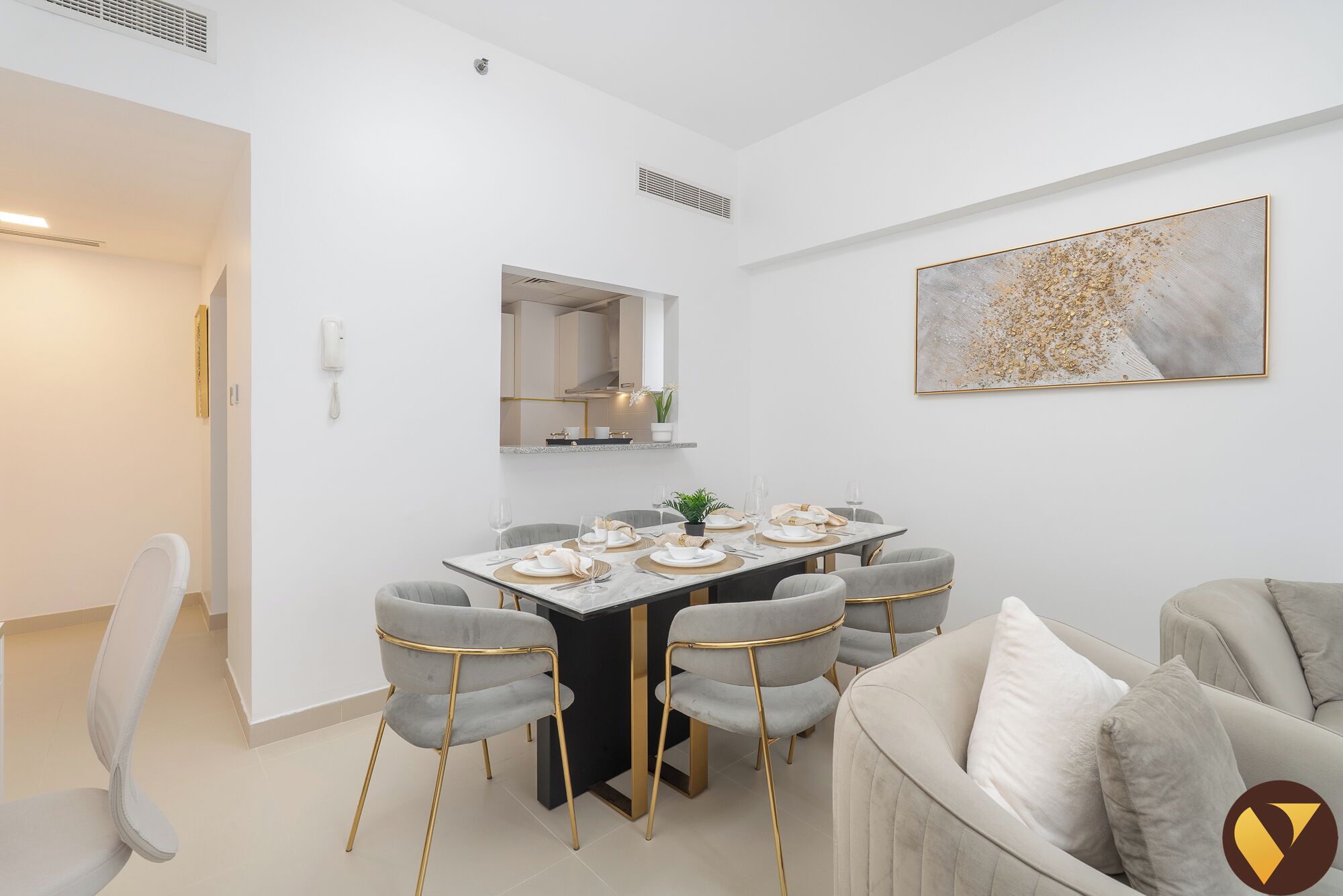 Un comedor moderno con una mesa blanca dispuesta para seis comensales, rodeada de sillas grises tapizadas con detalles dorados.
