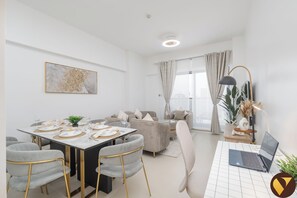 Una sala de estar moderna con comedor, un conjunto de sofá, una laptop sobre una mesa y un gran ventanal con cortinas.