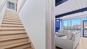 Una escalera de madera conduce a una habitación con un sofá blanco y vistas al exterior.