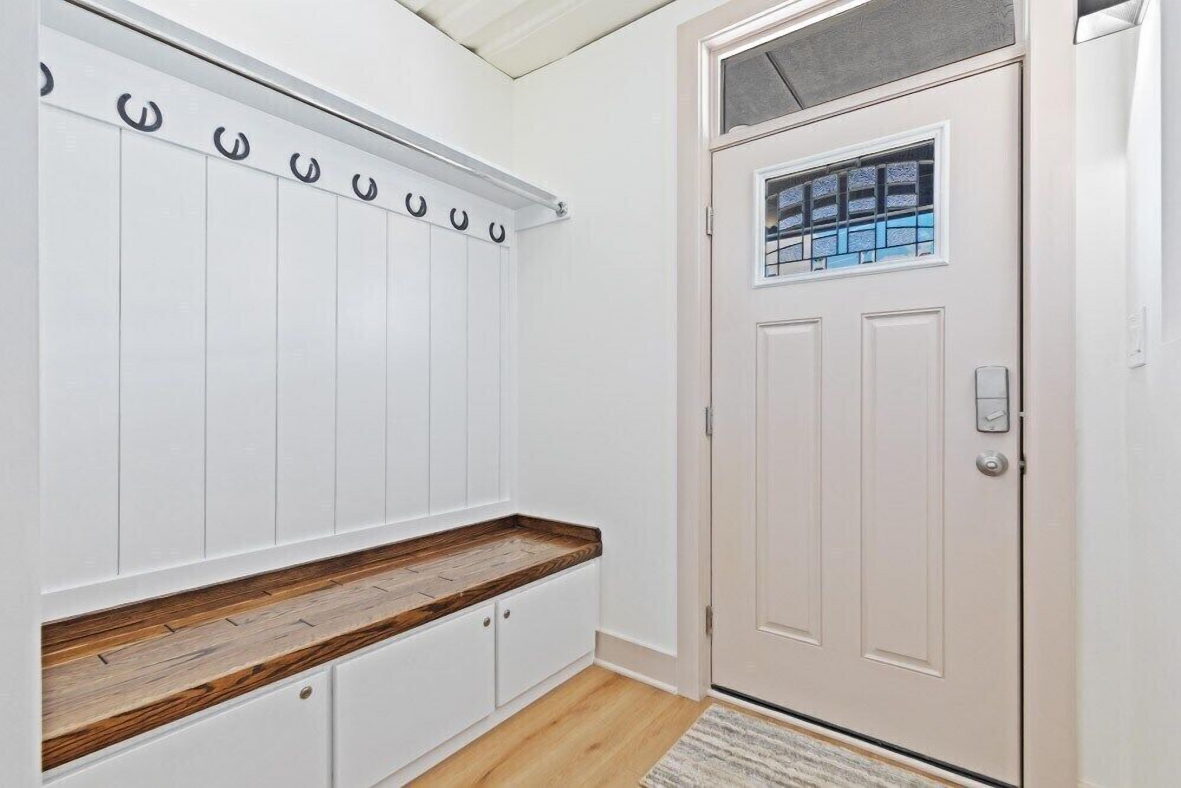 A hallway with a coat rack, a wooden bench, and a door with a window.