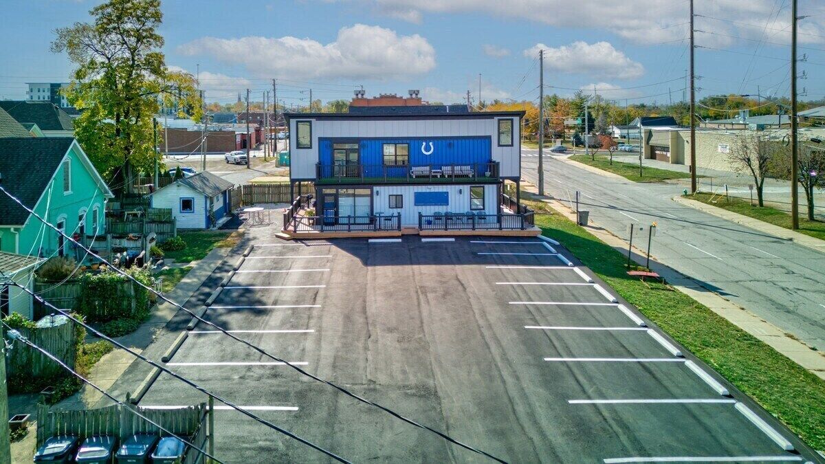 A modern building with a blue and white exterior, a parking lot in front, and a clear sky.