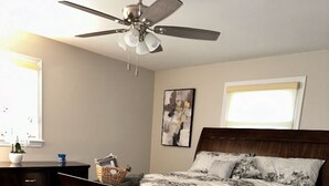 A bedroom with a wooden bed, a ceiling fan, a window with blinds, a bedside table with a lamp, and a wall-mounted artwork. - Spacious 4-bedroom house in nice Oxon Hill with WiFi, fitness room (Oxon Hill)