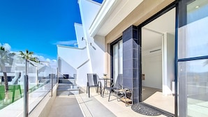 A modern building with a glass door entrance, a small outdoor seating area with chairs and a table, and a clear view of the sky. - Penthouse with private roof terrace (Mar de Cristal)