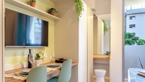 A modern dining area with a flat-screen TV, wooden table, two chairs, and a small potted plant. - Moderno-Pinheiros -AC - Brazilian Corner (São Paulo)