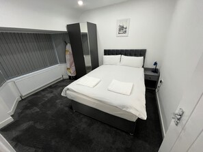 Relax in comfort with a large bed, bedside table, and window with blinds.