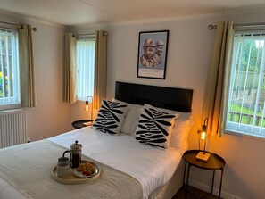 A neatly made bed with a tray of breakfast items, a framed picture on the wall, and a view of the outdoors through the windows. - Cosy Helvellyn Lodge With Wood Fired Hot Tub (Natland)