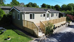 A single-story mobile home with a front deck, a small porch, and a gravel driveway.