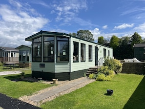 A mobile home with a large windowed front section, a small porch, and a well-maintained lawn.