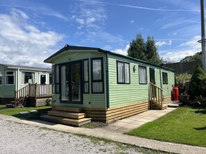 A single-story mobile home with a front porch, a small deck, and a paved driveway. - Cosy Helvellyn Lodge With Wood Fired Hot Tub (Natland)