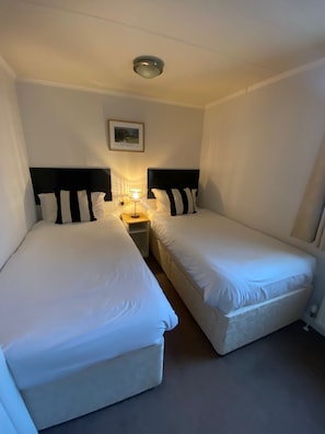 A small hotel room with two single beds, a nightstand with a lamp, and a ceiling light.