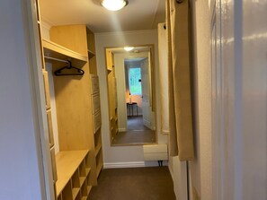 A narrow hallway with wooden shelving units on the left, a door at the end, and a window with curtains on the right.