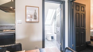 Ett modernt kök med en matplats, en inramad tavla på väggen och utsikt in i det intilliggande badrummet.