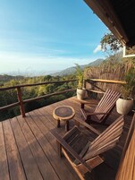 Una terraza de madera con una silla de madera y una mesita redonda, rodeada de vallas de bambú y plantas en macetas.