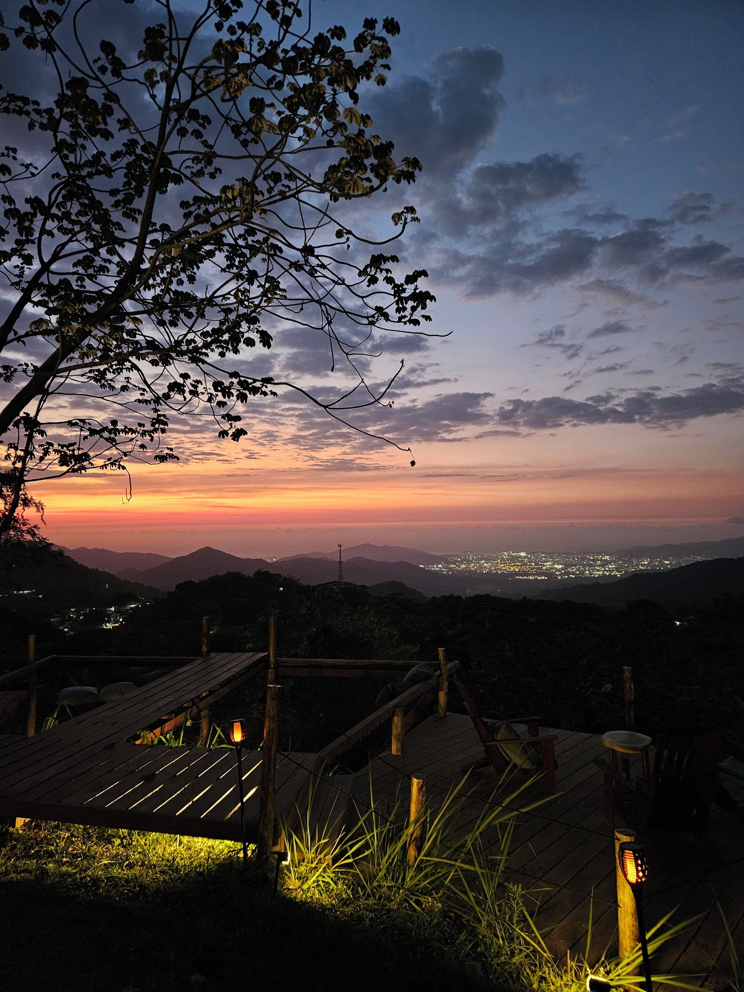 A wooden staircase leading to a viewing platform with a sunset view over a cityscape.