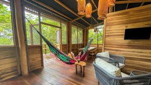 Una cabaña de madera con una hamaca, muebles de mimbre y ventanas amplias.
