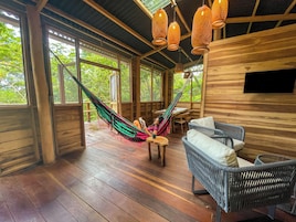 Una cabaña de madera con una hamaca, muebles de mimbre y ventanas amplias.
