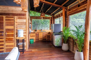 Interior de una cabaña de madera con cocina, comedor y ventanas amplias.