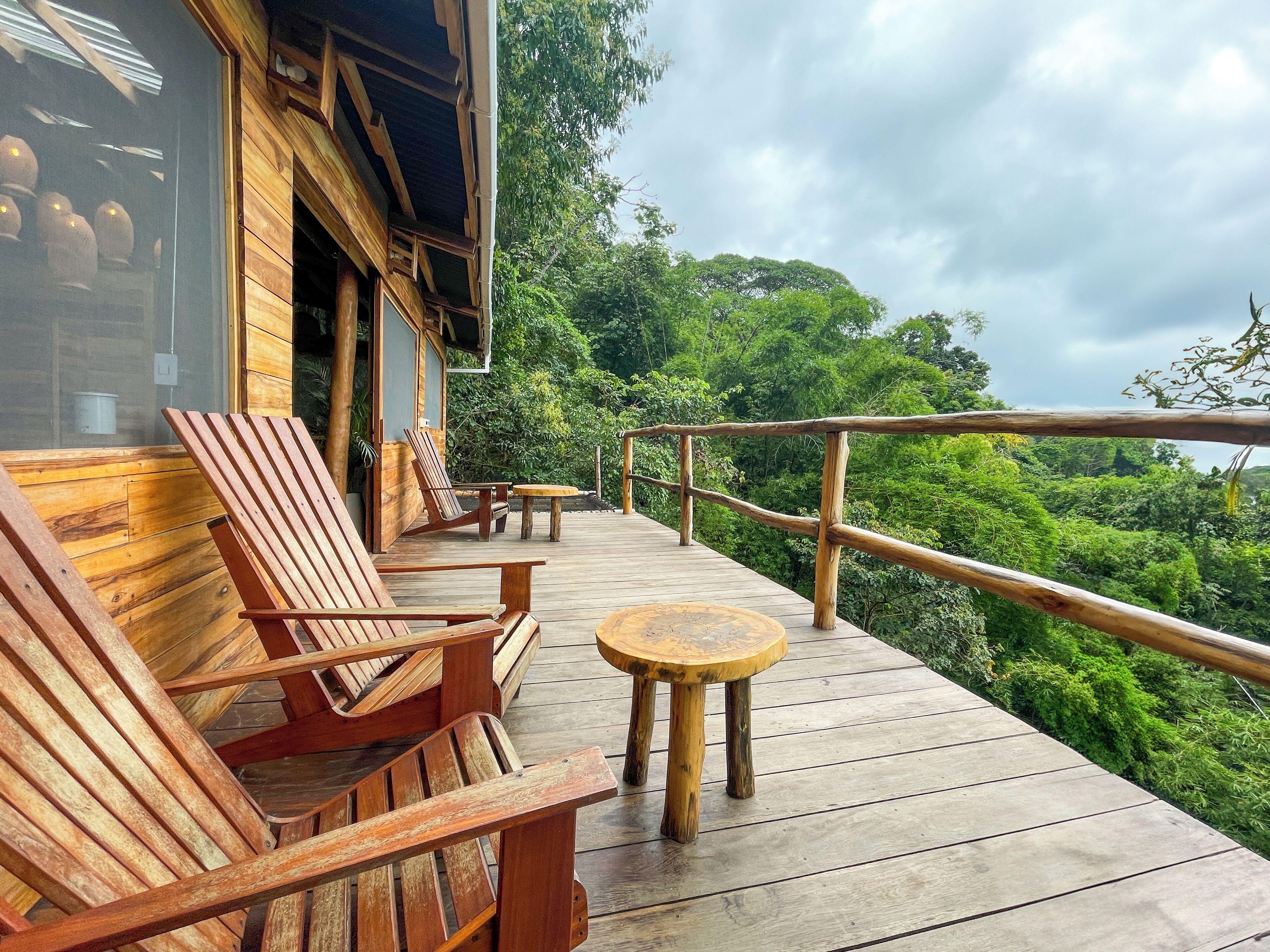 A wooden deck with chairs and tables, overlooking a lush forest.