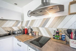 Una cucina moderna con piano cottura integrato, un tagliere di legno, una spechiera e un bollitore.