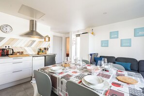 Una cucina moderna con cappa in acciaio inossidabile, un tavolo da pranzo apparecchiato con piatti, bicchieri e posate, e un angolo soggiorno con divano e cuscini blu.
